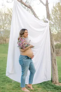 A pregnant woman holds her belly while holding flowers