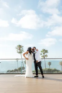 Bride and groom kissing with palm trees and ocean in back in San Diego