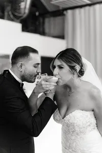 The bride and groom drink from their cocktail glasses together, sharing a quiet and happy moment after the ceremony, both dressed elegantly.