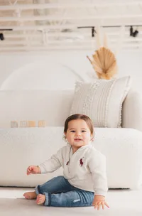 A baby boy smiles in front of a couch.
