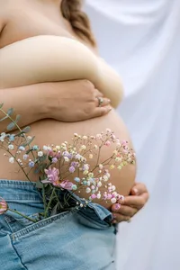 A pregnant woman holds her belly while holding flowers