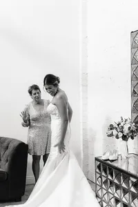 A black-and-white shot of the bride and her mother, who is wearing a sparkly dress, as they share a laugh while the bride finishes getting dressed.