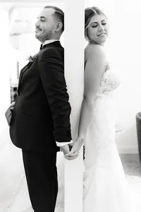 Black and white portrait of the bride and groom holding hands, each facing away but connected, capturing an intimate pre-ceremony moment.