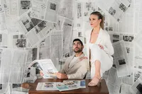 A couple is at a desk with a newspaper background
