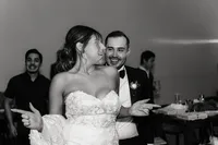 In a black-and-white photo, the bride and groom dance happily together, with the groom grinning and the bride animatedly enjoying the moment.