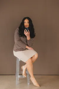 A woman sitting on a stool, casually using her phone with a relaxed expression.