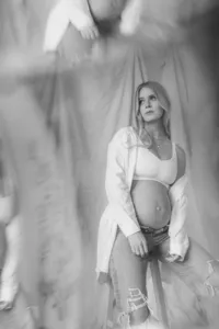 A pregnant woman poses on a stool with jeans