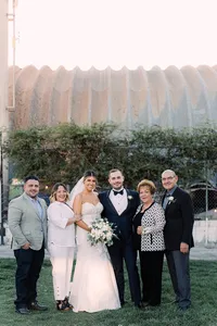 The bride and groom stand together, surrounded by family members in a casual, relaxed pose.