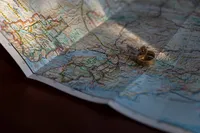 Two gold wedding rings rest on a folded map of Alaska, highlighted by a beam of sunlight.