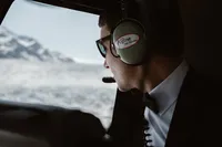 Groom in sunglasses and a helicopter headset looks out the window at the sprawling Alaska glacier below.