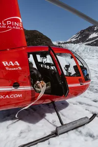 Red helicopter rests on an Alaska glacier with the bride’s bouquet and trailing ribbon visible through the open door.