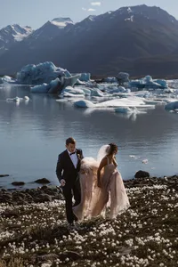 Newlyweds walk along the rocky shore of an Alaska glacial lake filled with blue-white icebergs.