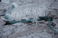 Aerial view of turquoise meltwater winding through the cracked white surface of an Alaska glacier.