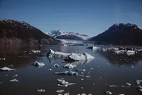 Icebergs float across a remote glacial lake, with a sprawling Alaska glacier and snow-covered mountains in the distance.