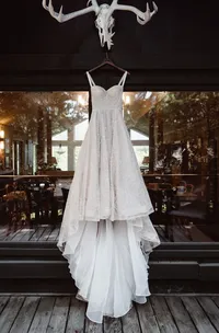 White lace wedding dress hangs in front of large cabin windows overlooking the surrounding Alaska forest.