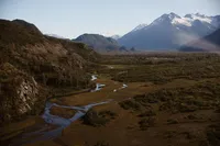 Winding streams weave through a broad Alaska valley beneath rugged, snow-dusted mountains.