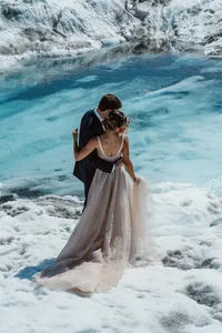 Bride and groom embrace beside brilliant turquoise glacial water, surrounded by the textured ice of an Alaska glacier.