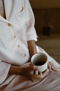 Bride in a white button-up pajama set holds a mug of coffee while getting ready for her Alaska elopement.