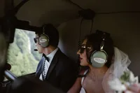 Bride and groom wear headsets and sunglasses inside the helicopter, looking out at the Alaska landscape during their flight.