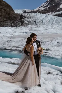 Bride and groom embrace on the glacier beside a vivid turquoise meltwater stream, surrounded by rugged ice.