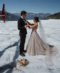 Bride adjusts the groom’s boutonniere as they stand together on an Alaska glacier, surrounded by rugged mountains.
