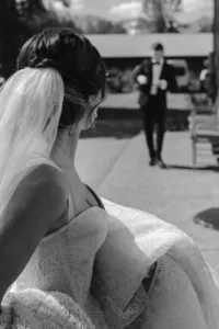 Black-and-white photo of the bride gathering her wedding dress as she walks toward the groom before their helicopter flight.