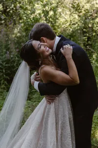 Groom hugs and kisses the smiling bride during their emotional first look in the Alaska forest.