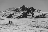 Black-and-white wide view of the newlyweds crossing a vast Alaska glacier beneath towering, snow-covered mountains.