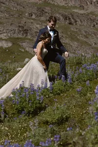 Bride and groom walk together through a mountainside meadow filled with purple wildflowers during their Alaska elopement.