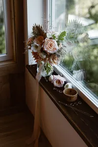 Blush and white bridal bouquet, loose flowers, rings and hairpins arranged on a cabin windowsill.