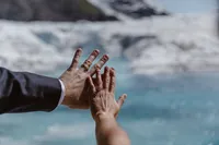 Newlyweds hold up their hands to show their wedding rings, with brilliant blue glacier ice blurred in the background.