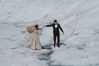Bride and groom hold hands as they carefully cross a crevasse on a remote Alaska glacier.