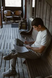 Groom sits on a wooden cabin porch, writing his private vows before the Alaska elopement.