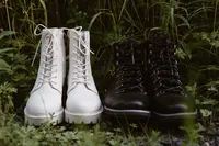 White lace-up boots and black leather boots sit side by side in the grass, ready for the Alaska elopement.