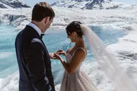 Bride places a wedding ring on the groom’s finger beside a vivid blue meltwater pool on an Alaska glacier.