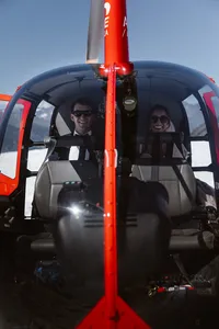 Smiling bride and groom wearing sunglasses sit side by side inside a red helicopter as they fly over an Alaska glacier.