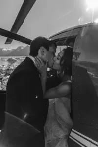 Black-and-white photo of the newlyweds kissing beside their helicopter after exploring the remote Alaska landscape.