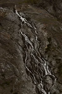 Aerial view of cascading streams weaving down a steep, rocky mountainside in the Alaska wilderness.