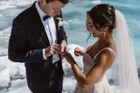 Groom places a wedding ring on the bride’s finger during their private ceremony on an Alaska glacier.