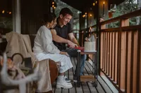 Bride and groom sit together on a cozy cabin porch, smiling as they cut into a small cake after their Alaska elopement.