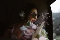 Bride wearing sunglasses and a helicopter headset looks out the window, her blush floral bouquet filling the foreground.