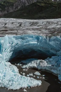 Aerial view of a deep blue ice cave carved into an Alaska glacier, surrounded by fractured ice and meltwater.