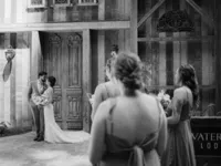 bridesmaids watching bride and groom take their wedding portraits by the barn