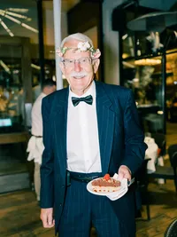 grandpa wearing flower crown and carrying piece of cake during wedding reception
