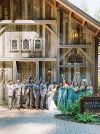 bridal party cheering on bride and groom in front of waterfall lodge barn