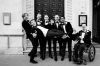 fun formal photo of groom being held by groomsmen including one in wheelchair