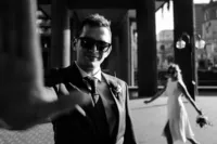 unique creative wedding photo of groom holding his hand up and bride walking in the background taken in east london barbican