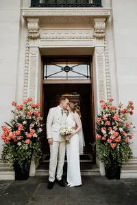 bride and groom in summer light suit kissing between flowers outside marylebone town halll entrance