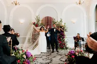andaz wedding ceremony with bride and groom holding hands in the air in front of floral arch