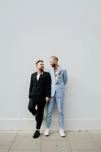 two grooms posing and looking at each other wearing fashion forward modern suits blue and black for their same sex wedding in hoxton hotel